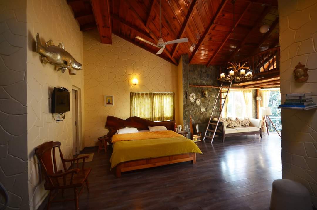 Spacious bedroom with a timber ceiling, a yellow-draped bed, stone walls and a ladder up to the loft