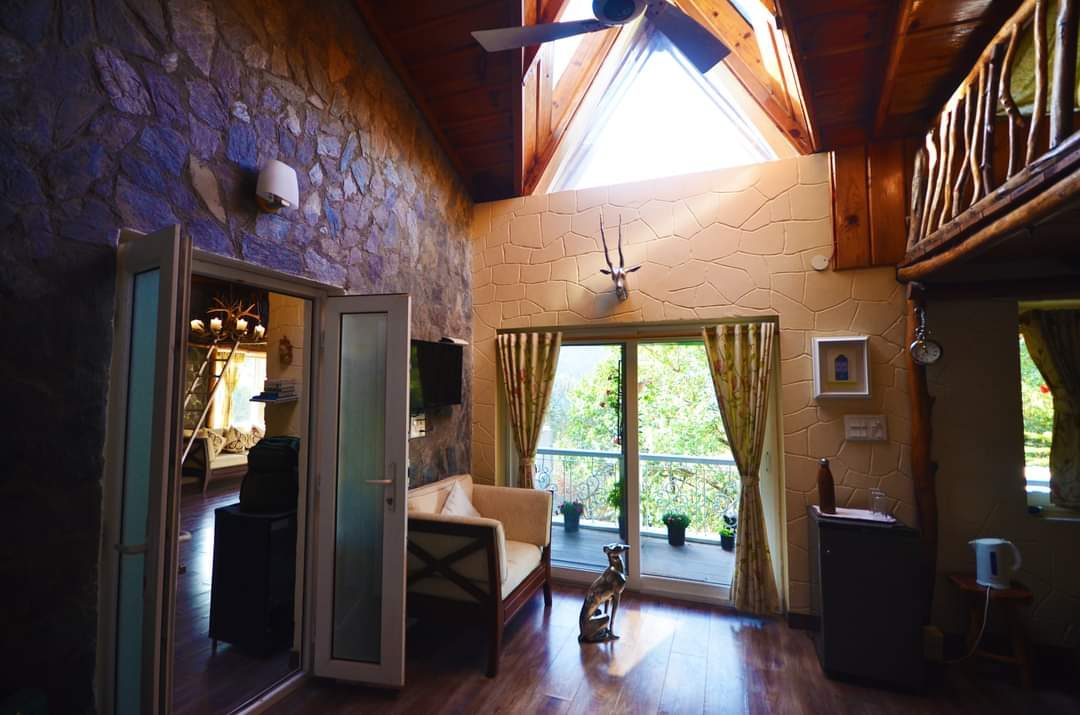 Room with a stone wall, a triangular gable window and a branch-railed loft above