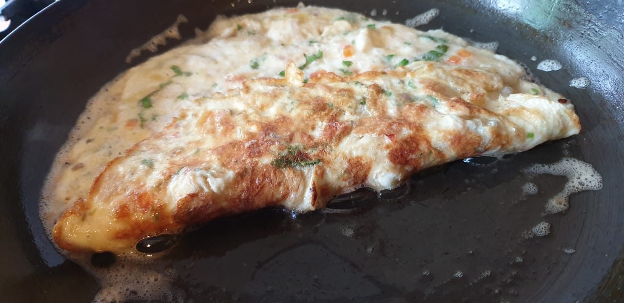A golden omelette cooking in a black pan