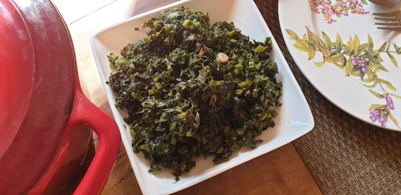 A dish of sautéed leafy greens beside a red cast-iron pot