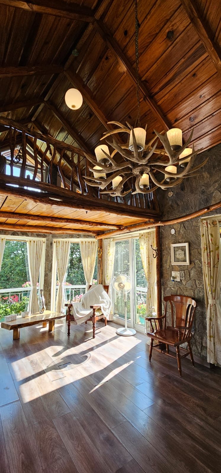 Sunlight across wooden floors under a pitched timber ceiling and an antler chandelier