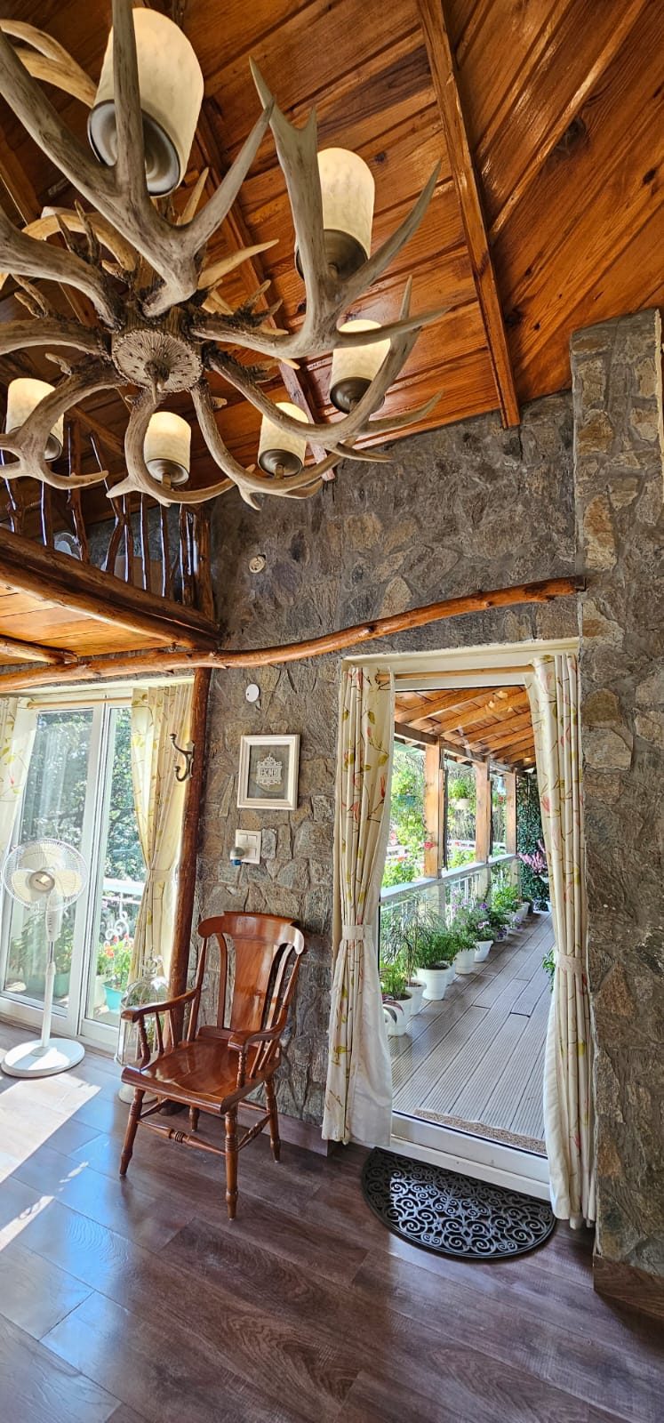 An antler chandelier and stone wall framing a doorway onto a plant-lined verandah