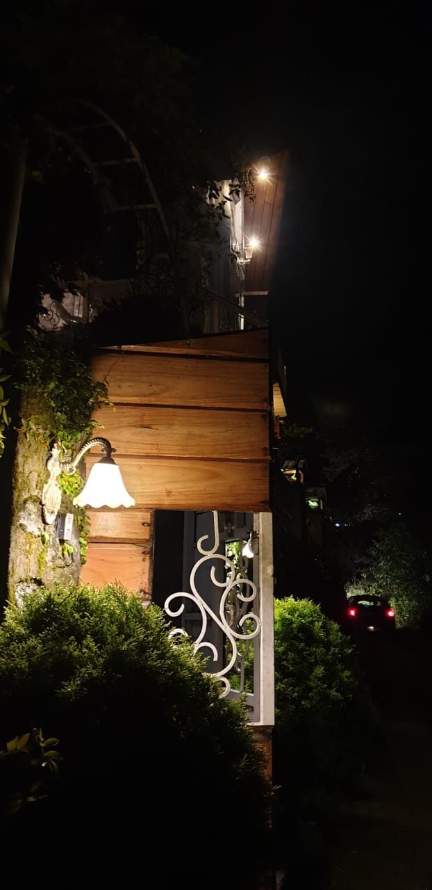 A wall lantern glowing beside the wooden entrance gate at night