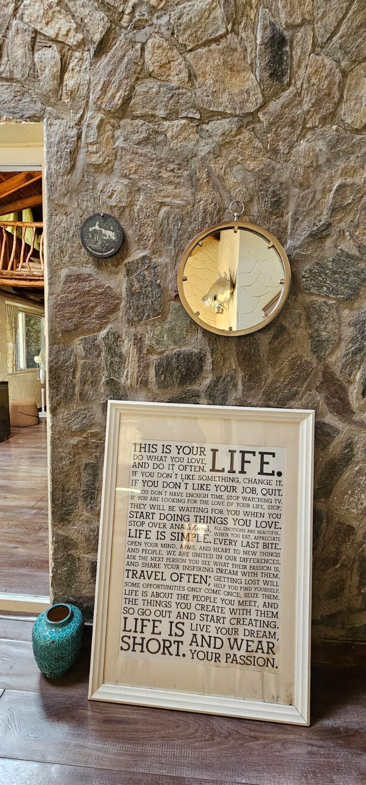 Hand-laid stone wall with a brass clock and a framed print resting on the wooden floor